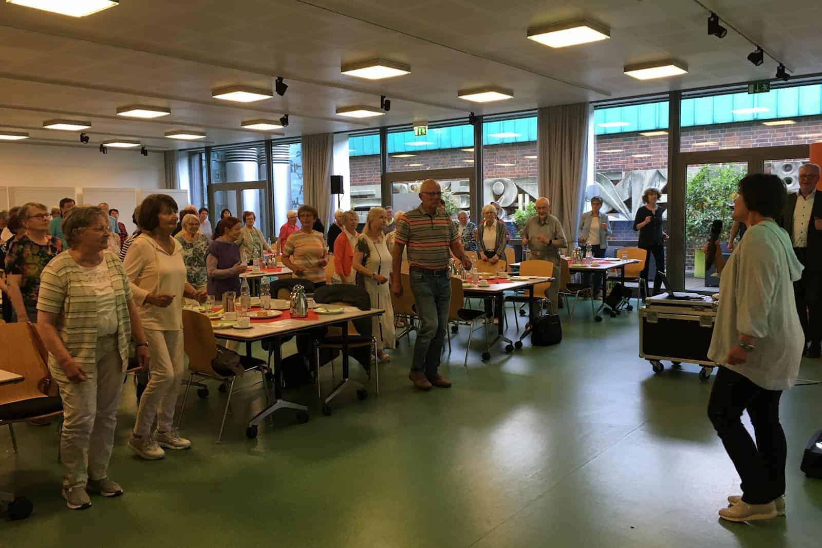 Im komplett gefüllten Saal führt eine Therapeutin Übungen vor und das Publikum macht stehend mit.