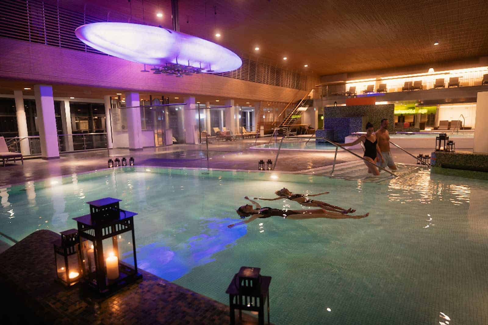 Menschen liegen in einem Thermalbad bei Kerzenlicht und genießen die Wärme.
