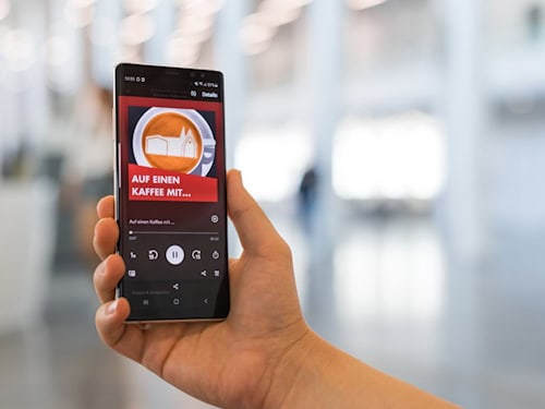 Das Logo des Wissenschaftspodcasts „Auf einen Kaffee mit …“ der Universität Leipzig ist auf einem Smartphone zu sehen.