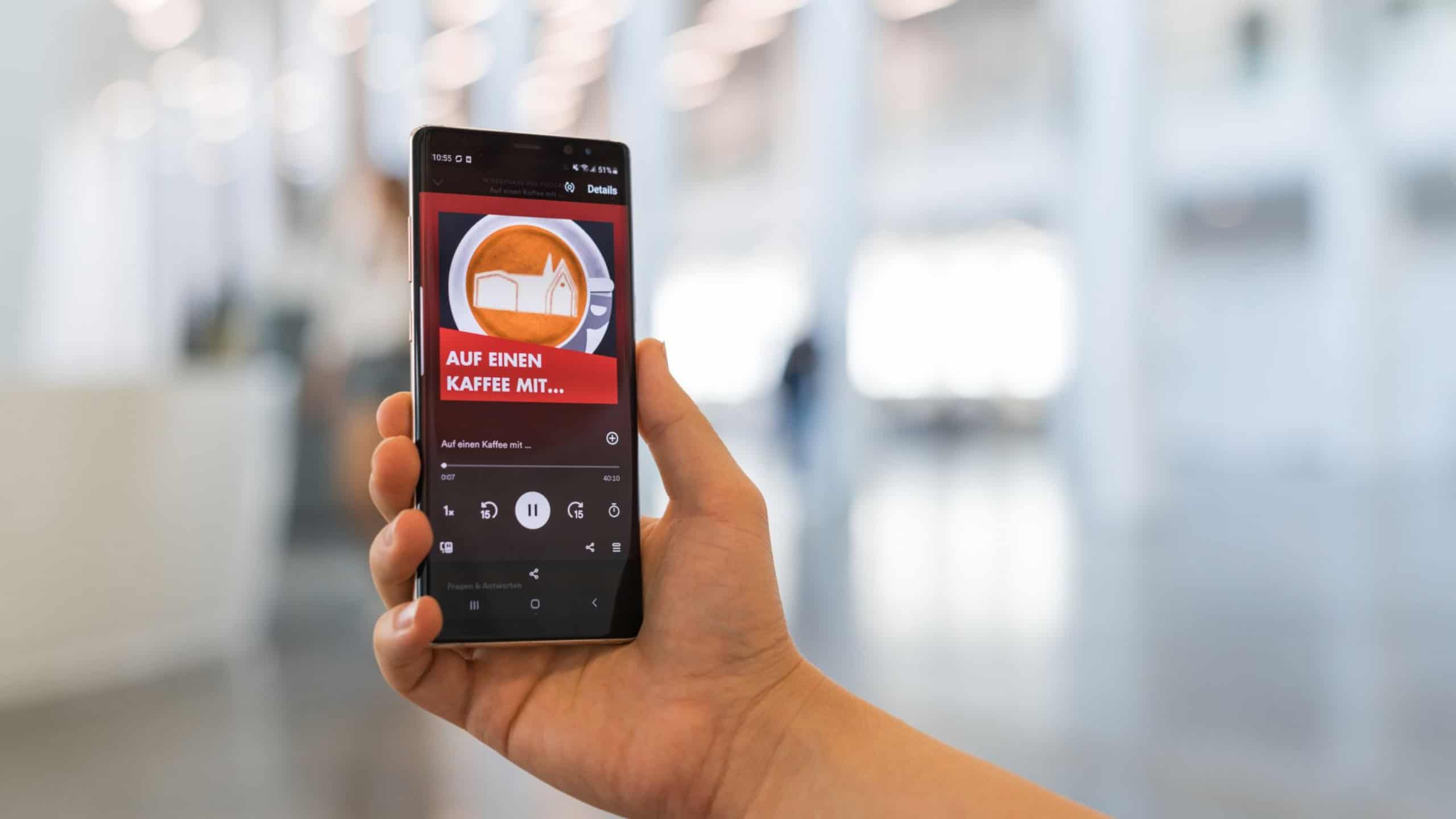 Das Logo des Wissenschaftspodcasts „Auf einen Kaffee mit …“ der Universität Leipzig ist auf einem Smartphone zu sehen.