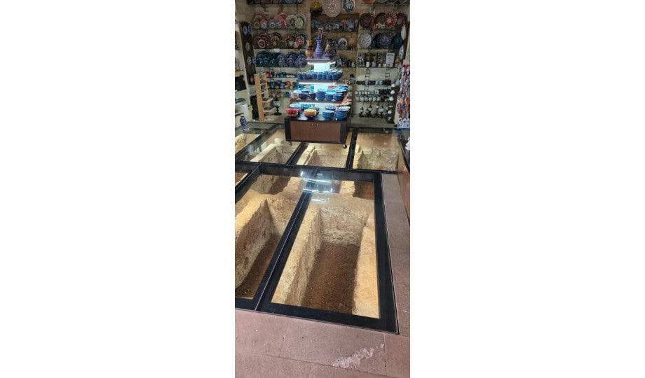 Denkmalschutz Immobilienbewertung: Blick auf mehrere Grabstellen unter Glasplatten zwischen Ladenregalen.