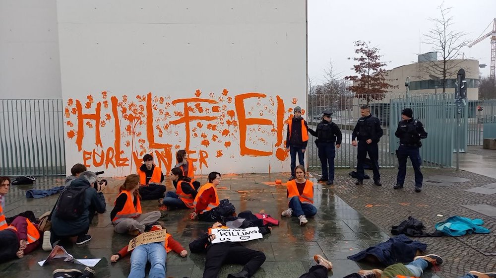 Aktivistinnen und Aktivisten der Letzten Generation sitzen vor einer Wand des Bundeskanzleramts. / Foto: Letzte Generation/dpa