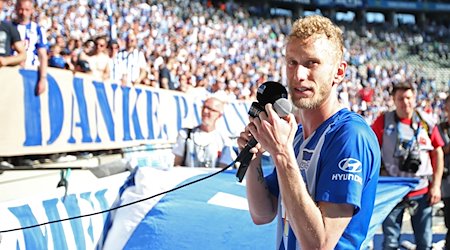 Fabian Lustenberger von Hertha BSC steht mit zwei Mikrofonen in der Hand gerührt vor der Fankurve. / Foto: Andreas Gora/dpa/Archivbild