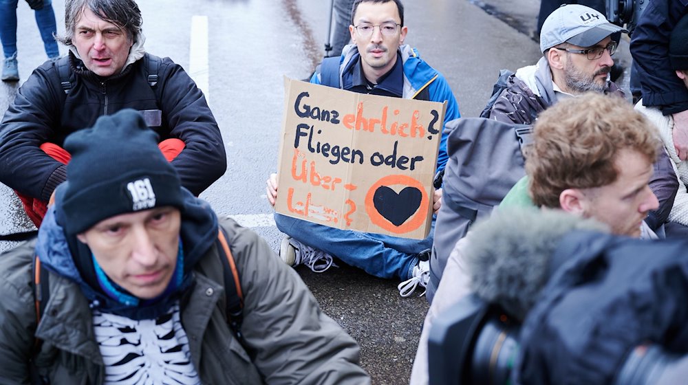 „Ganz ehrlich? Fliegen oder Überleben“ steht auf einem Plakat, das ein Klimaaktivist hält. / Foto: Annette Riedl/dpa