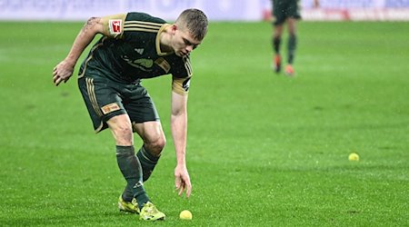 Andras Schäfer von Union hebt einen Tennisball auf, der aus dem Block der Union-Fans geworfen wurde. / Foto: Arne Dedert/dpa