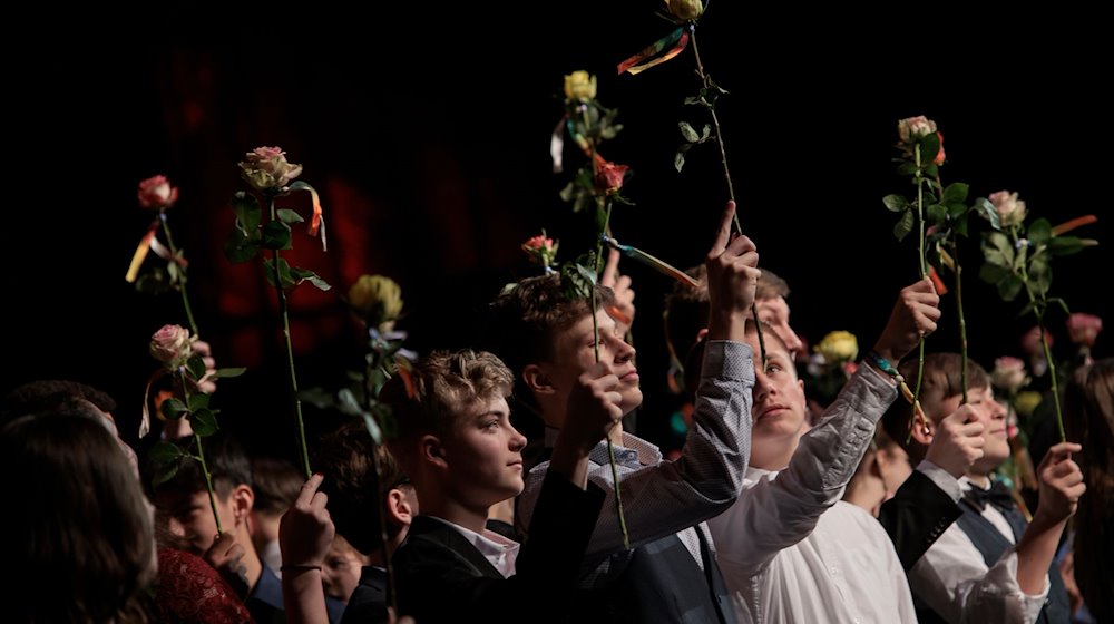 Teilnehmer der Jugendfeier des Humanistischen Verbands Berlin-Brandenburg schwenken Rosen auf der Bühne bei der Festveranstaltung. / Foto: Carsten Koall/dpa
