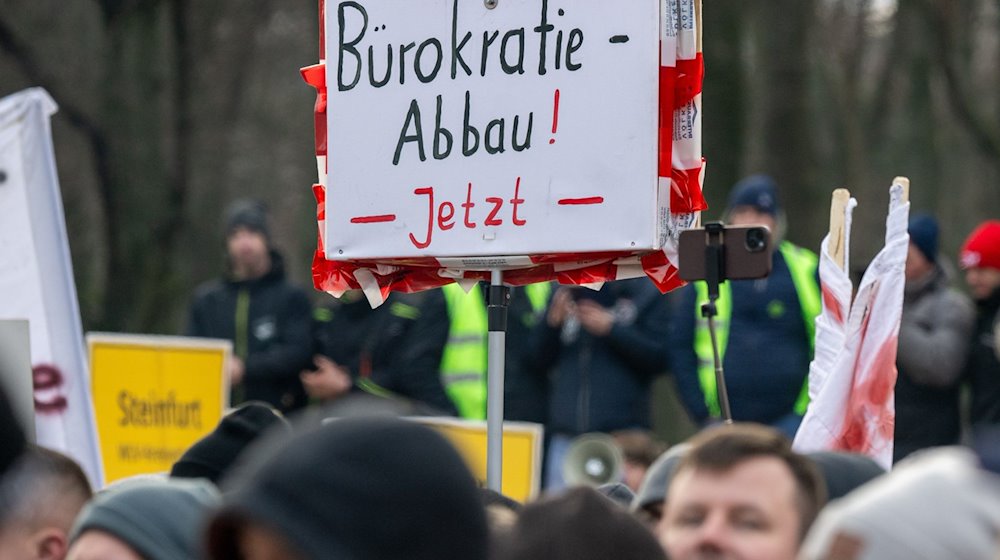 Ein Landwirt hält während der Kundgebung vor dem Brandenburger Tor ein Schild mit der Aufschrift «Bürokratie-Abbau! Jetzt» hoch. / Foto: Monika Skolimowska/dpa