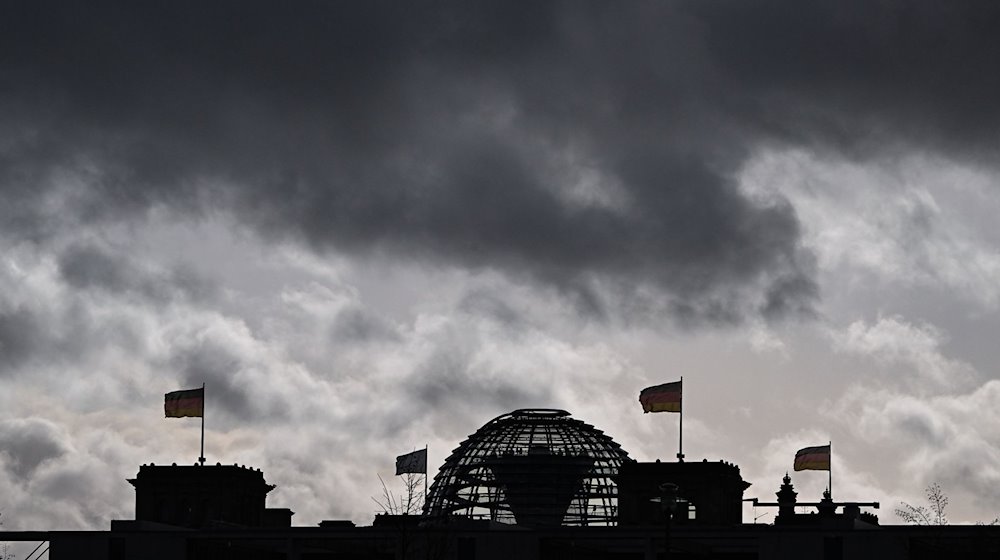 Wolken sind über der Kuppel vom Reichstag zu sehen, auf dem Deutschlandfahnen wehen. / Foto: Jens Kalaene/dpa