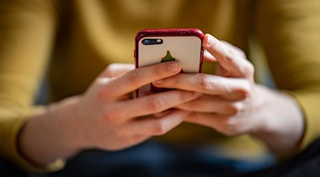 Eine junge Frau hält ein Smartphone in der Hand. / Foto: Fabian Sommer/dpa/Illustration