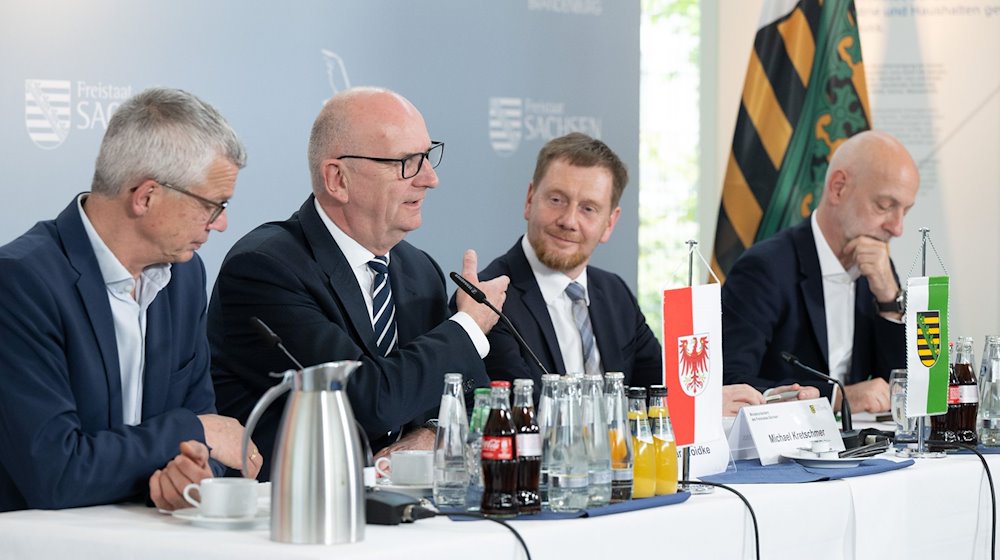 Florian Engels (l-r), Regierungssprecher, Dietmar Woidke (SPD), Ministerpräsident von Brandenburg, Michael Kretschmer (CDU), Ministerpräsident von Sachsen, und Ralph Schreiber, Regierungssprecher, nehmen nach einer bilateralen Kabinettssitzung im Kraftwerk Boxberg an einer Pressekonferenz teil. / Foto: Sebastian Kahnert/dpa