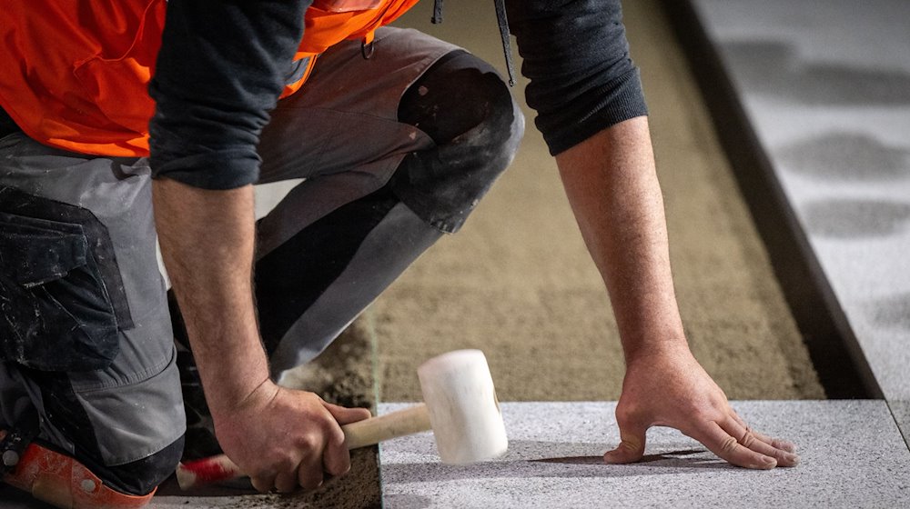 Ein Bauarbeiter verlegt mit einem Gummihammer den Bodenbelag auf einer Baustelle. / Foto: Monika Skolimowska/dpa/Symbolbild