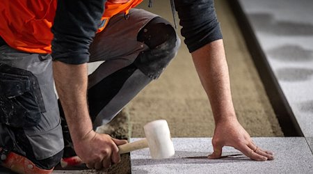 Ein Bauarbeiter verlegt mit einem Gummihammer den Bodenbelag auf einer Baustelle. / Foto: Monika Skolimowska/dpa/Symbolbild