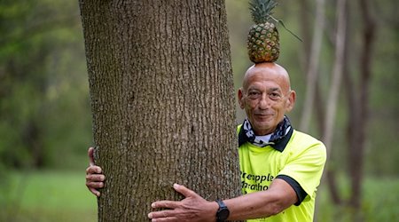 Moshe Lederfien, ein israelischer Marathon-Läufer, der bei seinen Läufen stets eine Ananas auf dem Kopf trägt, umarmt einen Baum im Tiergarten. / Foto: Monika Skolimowska/dpa