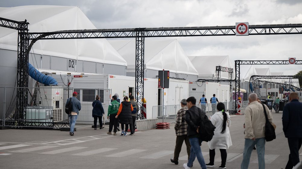 Bewohner und Mitarbeiter gehen im Ankunftszentrum am ehemaligen Flughafen Tegel in Richtung der Leichtbauhallen. / Foto: Sebastian Gollnow/dpa