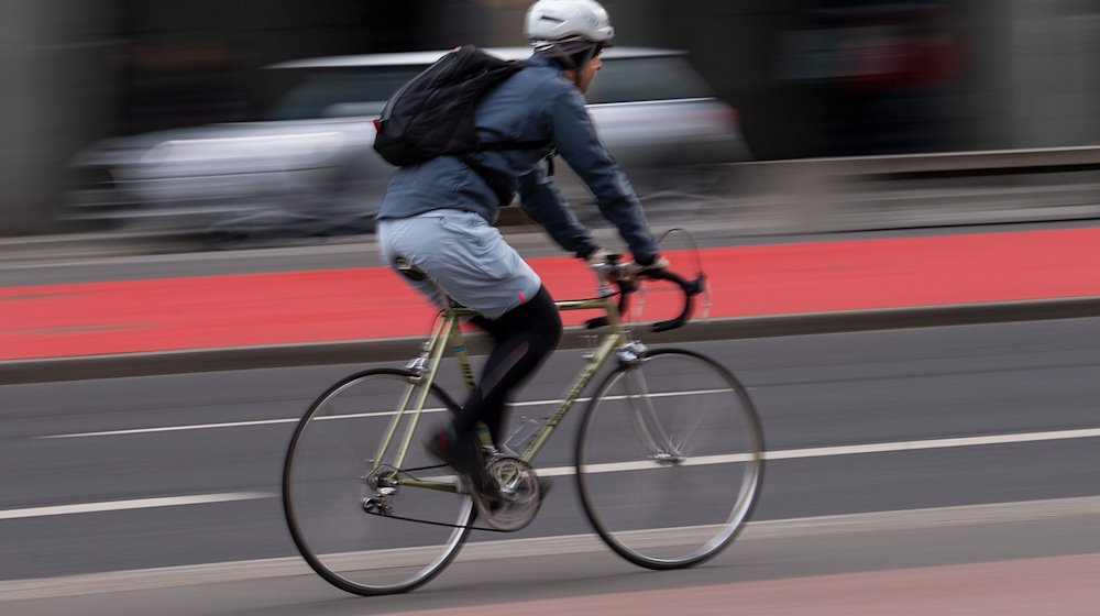 Ein Fahrradfahrer mit Helm fährt über einen Radweg an der Straße. / Foto: Monika Skolimowska/dpa-Zentralbild/dpa