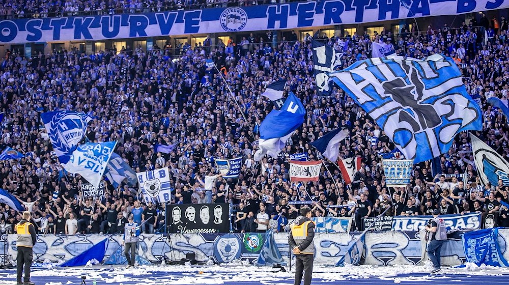 Fans von Hertha BSC feuern ihr Team aus der Ostkurve mit Fahnen an. / Foto: Andreas Gora/dpa