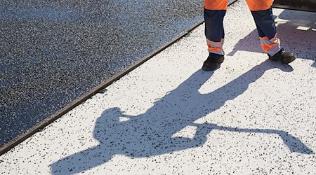 Der Schatten eines Bauarbeiters fällt auf den Boden einer Straße, die asphaltiert wird. / Foto: Thomas Frey/dpa