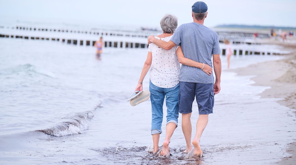 Ein Rentnerehepaar geht am Strand Arm in Arm spazieren. / Foto: Annette Riedl/dpa