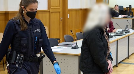 Ein mutmaßliches Mitglied der Terrorgruppe "Vereinte Patrioten" wird in den Verhandlungssaal gebracht. Den vier Männern im Alter zwischen 44 und 56 Jahren und einer Frau (im Bild) wird vorgeworfen, eine inländische terroristische Vereinigung gegründet zu haben oder darin Mitglied gewesen zu sein. / Foto: Thomas Frey/dpa POOL/dpa