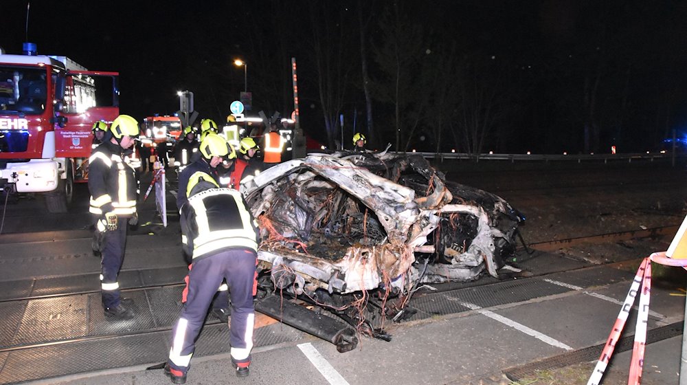 Rettungskräfte stehen am Wrack eines zerstörten Autos nach einem Unfall an einem Bahnübergang. / Foto: Christian Sappeck/BLP/dpa