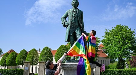 Am Denkmal von Kronprinz Friedrich zeigen der Politiker Freke Over und Marie von der Vorbereitungsgruppe des ersten "Christopher Street Day" (CSD) in Rheinsberg die Regenbogenfahne. / Foto: Jens Kalaene/dpa