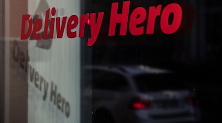 Das Logo und der Schriftzug des Essenslieferdienstes Delivery Hero spiegelt sich in einer Scheibe. / Foto: Paul Zinken/dpa