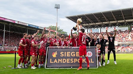 Jonas Hildebrandt von Energie Cottbus hält die Siegertrophäe in die Höhe und bejubelt den Landespokalsieg. / Foto: Sebastian Räppold/Matthias Koch/dpa