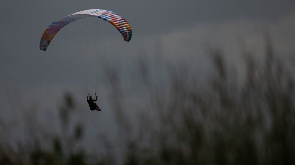 Ein Gleitschirmflieger wird von der Sonne angeschienen während er in einer Wiese landet. / Foto: Sebastian Gollnow/dpa