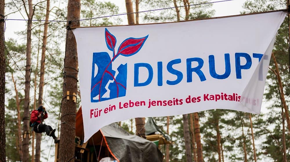 Ein Banner mit der Aufschrift  «Disrupt - für ein Leben jenseits des Kapitalismus» hängt im Camp der Initiative «Tesla stoppen» in einem Kiefernwald nahe der Tesla-Gigafactory Berlin-Brandenburg zwischen Bäumen. / Foto: Christoph Soeder/dpa/Archivbild