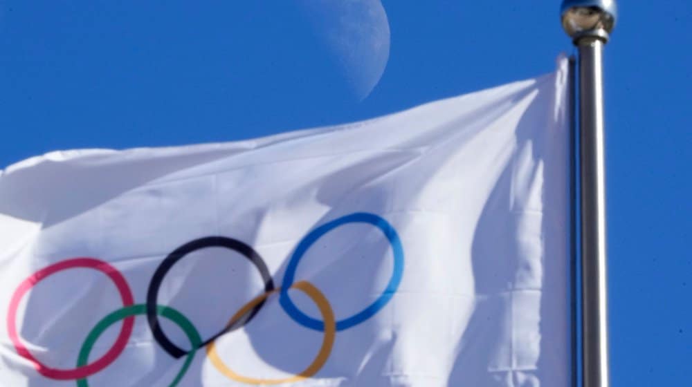 Eine olympischen Flagge weht vor blauem Himmel im Wind. / Foto: Dmitri Lovetsky/AP/dpa/Symbolbild