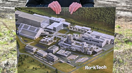 Ein Bild mit einer Computersimulation der fertigen Fabrik zeigt ein Mitarbeiter von Rock Tech auf dem Baugelände für eine Lithiumfabrik des kanadischen Unternehmens. / Foto: Patrick Pleul/dpa