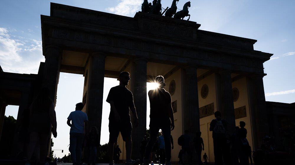 Touristen gehen im Gegenlicht der untergehenden Sonne über den Pariser Platz vor der Kulisse vom Brandenburger Tor. / Foto: Monika Skolimowska/dpa