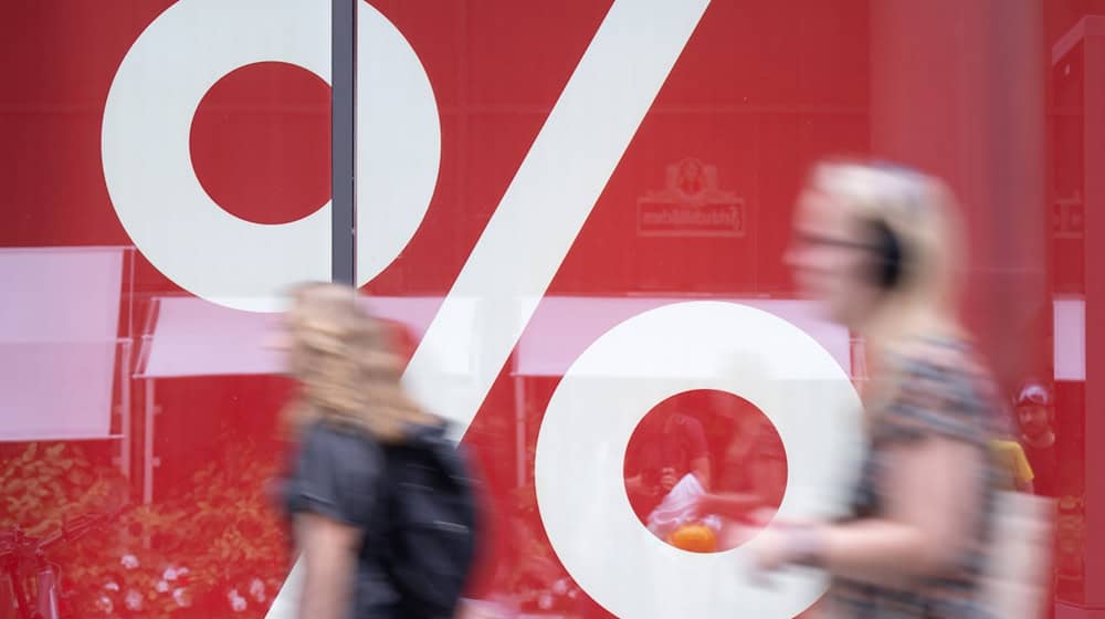 Passanten gehen in einer Fußgängerzone an einem Schaufenster eines Modegeschäfts vorbei, dass mit einer Rabattaktion wirbt. / Foto: Sebastian Kahnert/dpa