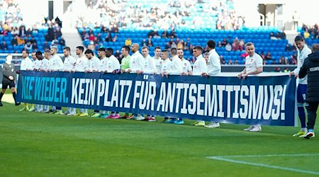 Hoffenheims Spieler halten vor Beginn des Spiels ein Transparent mit der Aufschrift „Nie wieder. Kein Platz für Antisemitismus“. / Foto: Uwe Anspach/dpa