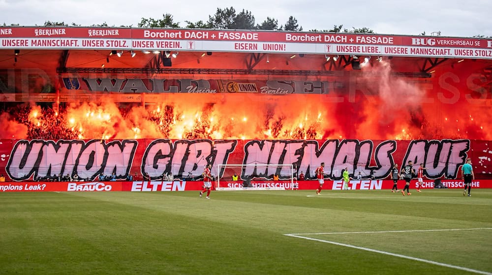 Fans von Union Berlin zünden Bengalisches Feuer auf der Waldseite hinter dem Schriftzug "Union gibt niemals auf!" Für das Abbrennen muss Union nun Strafe zahlen. / Foto: Andreas Gora/dpa