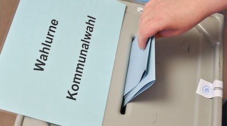 Eine Person steckt ihren Stimmzettel in eine Wahlurne mit der Aufschrift «Wahlurne Kommunalwahl». / Foto: Patrick Pleul/dpa