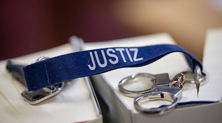 Ein Schlüsselanhänger mit dem Wort «Justiz» und Mini-Handschellen liegen auf zwei Gesetzbüchern. / Foto: Monika Skolimowska/dpa