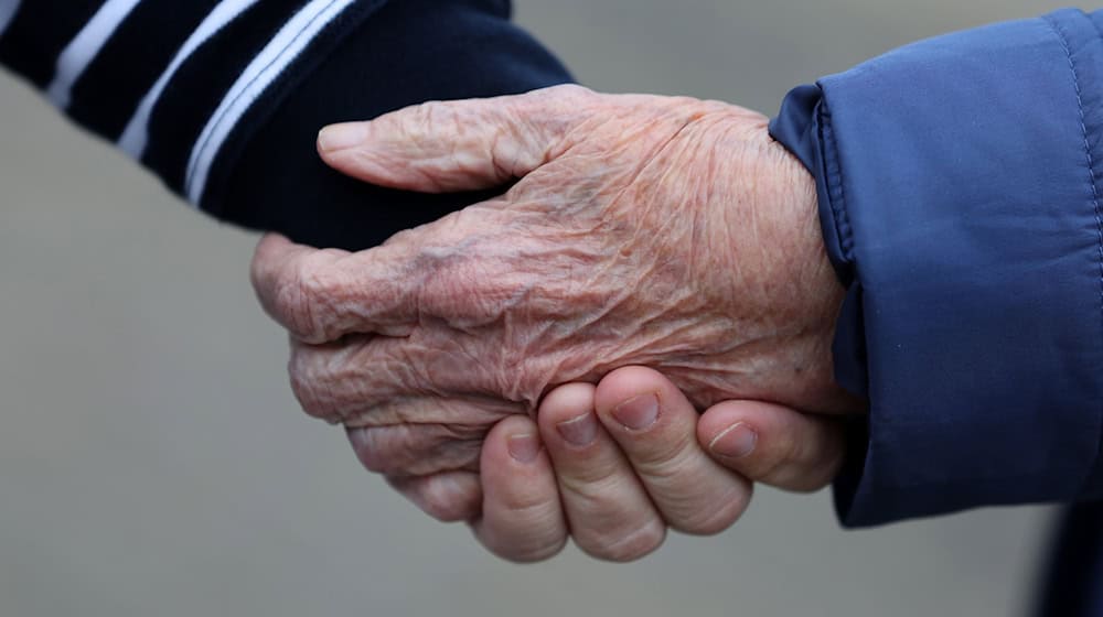 Eine Betreuungsassistentin hält die Hand von einer alten Frau. / Foto: Bernd Wüstneck/dpa