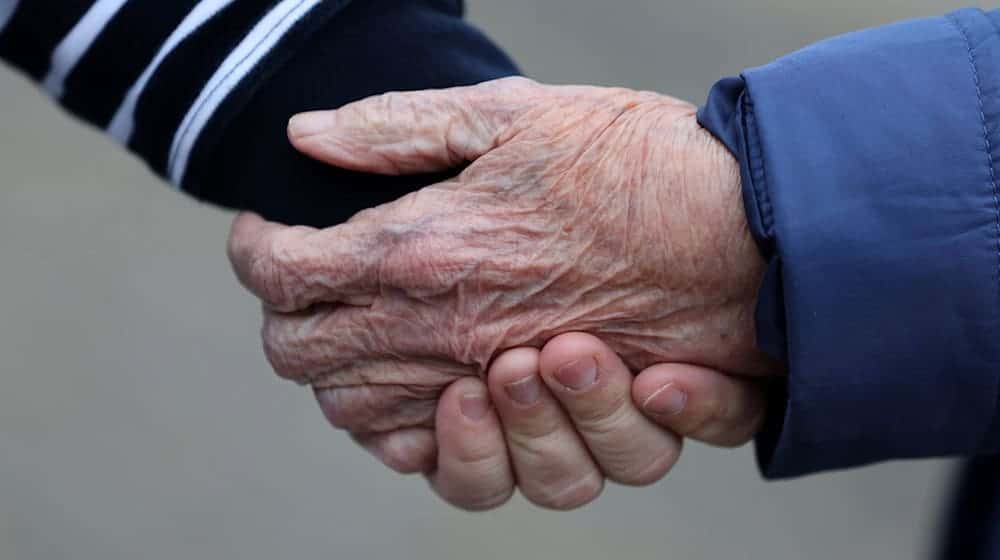 Eine Betreuungsassistentin hält die Hand von einer alten Frau. / Foto: Bernd Wüstneck/dpa