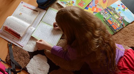 Ein Mädchen liegt auf einem Teppich in seinem Kinderzimmer und erledigt seine Hausaufgaben im Fach Deutsch. / Foto: Jens Kalaene/dpa-Zentralbild/dpa