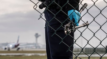 Eine Beamtin der Bundespolizei steht nach einer Protestaktion der «Letzten Generation» im Herbst 2022 mit einem sichergestellten Bolzenschneider an einem Zaun am Flughafen BER. / Foto: Paul Zinken/dpa