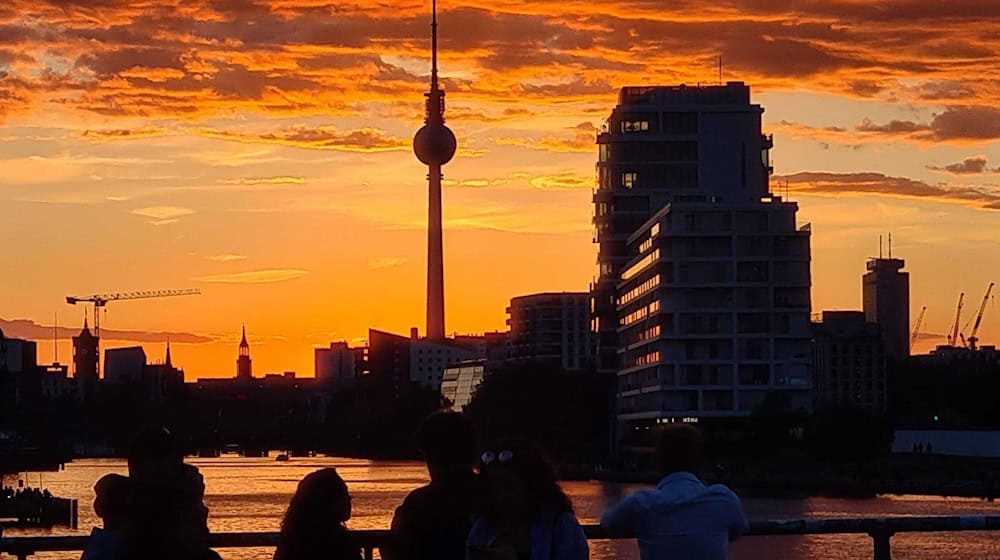 Menschen betrachten auf der Oberbaumbrücke den Sonnenuntergang über der Spree. Im Hintergrund ist der Fernsehturm zu sehen. (Archivbild) / Foto: Sophia Weimer/dpa