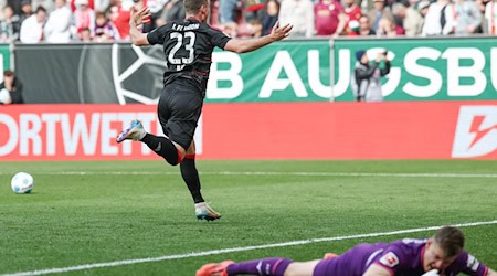 Berlins Matchwinner Andrej Ilic läuft nach seinem Siegtor jubelnd vor den Union-Fanblock. Augsburgs Torwart Finn Fahmen liegt geschlagen am Boden. / Foto: Daniel Löb/dpa