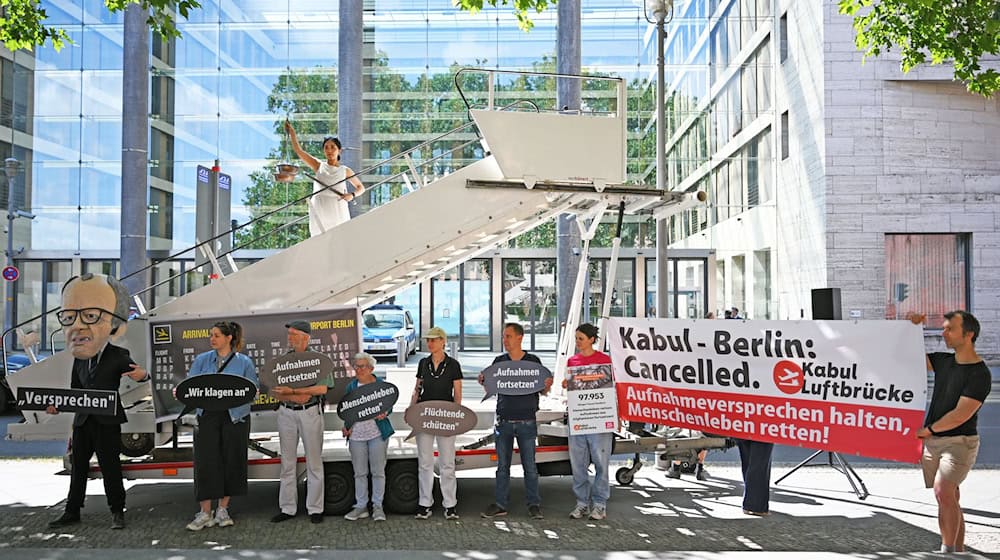 Aktivsten stehen während einer symbolischen Protestaktion am Weltflüchtlingstag zur Unterstützung mehrerer Klagen von Afghanen gegen die Bundesregierung vor dem Auswärtigen Amt. / Foto: Michael Brandt/dpa