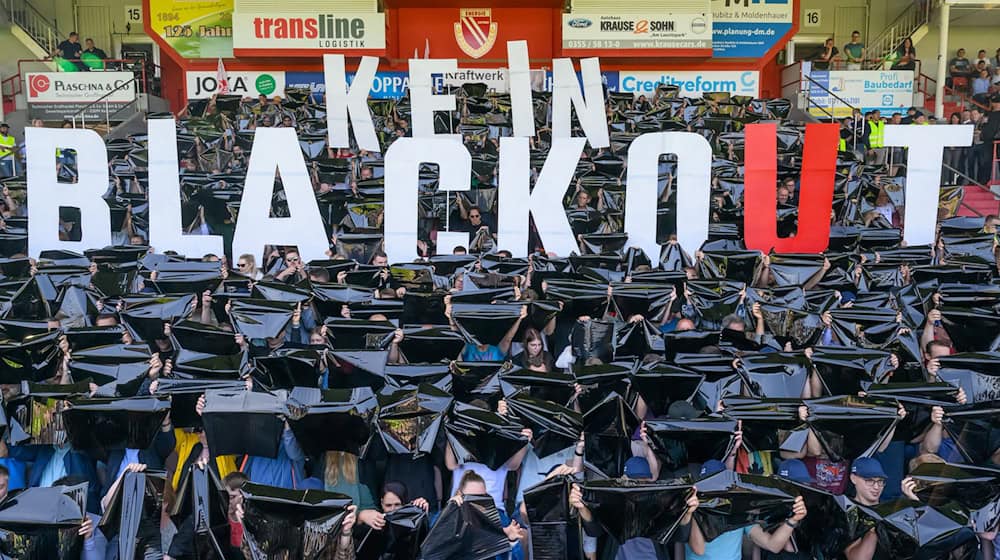 Leag-Beschäftigte halten bei einer Betriebsversammlung im Fußballstadion in Cottbus den Spruch «Kein Blackout» hoch.  / Foto: Patrick Pleul/dpa