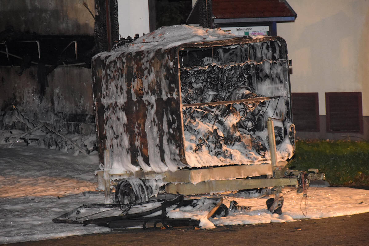 Verkohlter Anhänger mit Löschschaum bedeckt, steht auf gepflastertem Boden vor dem abgebrannten Gerätehaus. Verkohlter Anhänger mit Löschschaum bedeckt, steht auf gepflastertem Boden vor dem abgebrannten Gerätehaus.