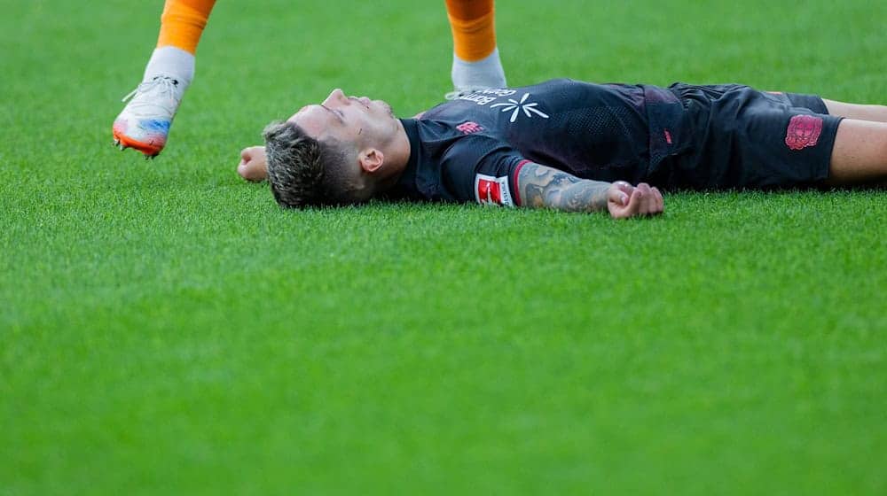 Bayer Leverkusens Kapitän Alejandro Grimaldo liegt nach einem Zusammenprall mit dem eigenen Mann benommen auf dem Boden.  / Foto: Rolf Vennenbernd/dpa