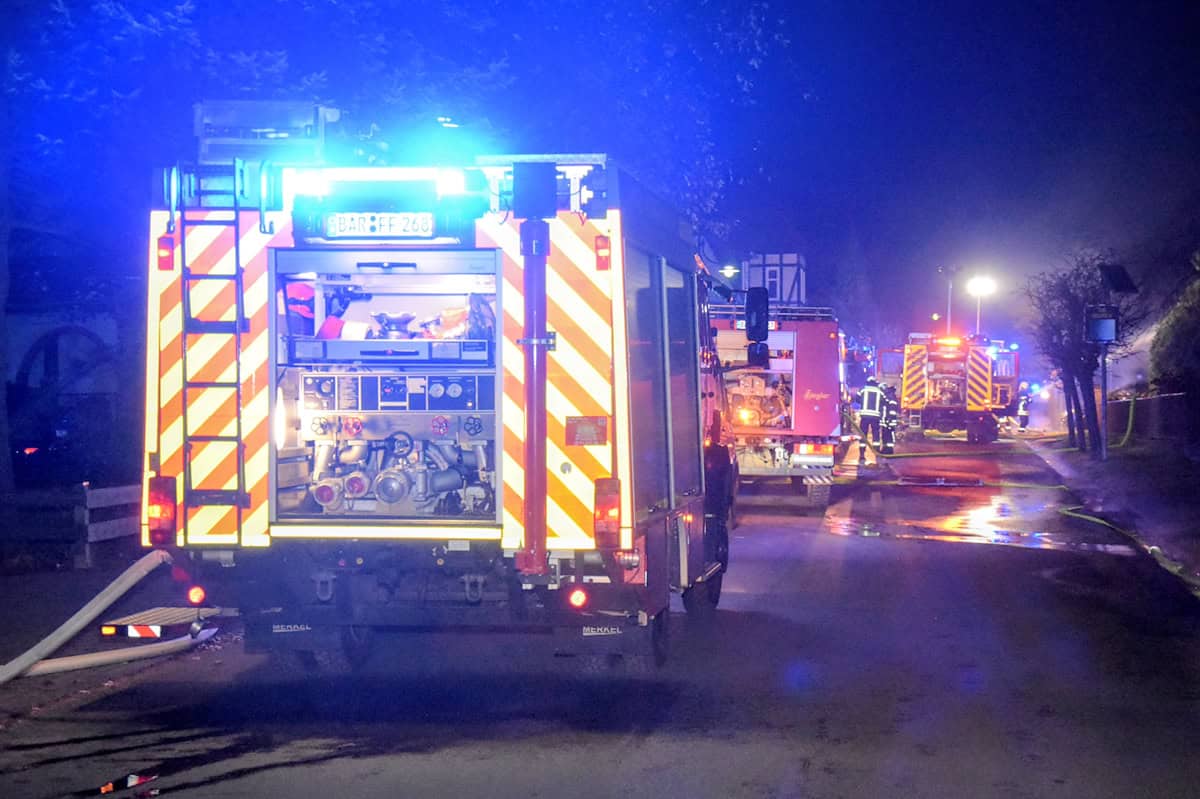 Mehrere Feuerwehrfahrzeuge mit eingeschalteten Blaulichtern stehen nachts auf einer nassen Straße. Mehrere Feuerwehrfahrzeuge mit eingeschalteten Blaulichtern stehen nachts auf einer nassen Straße.