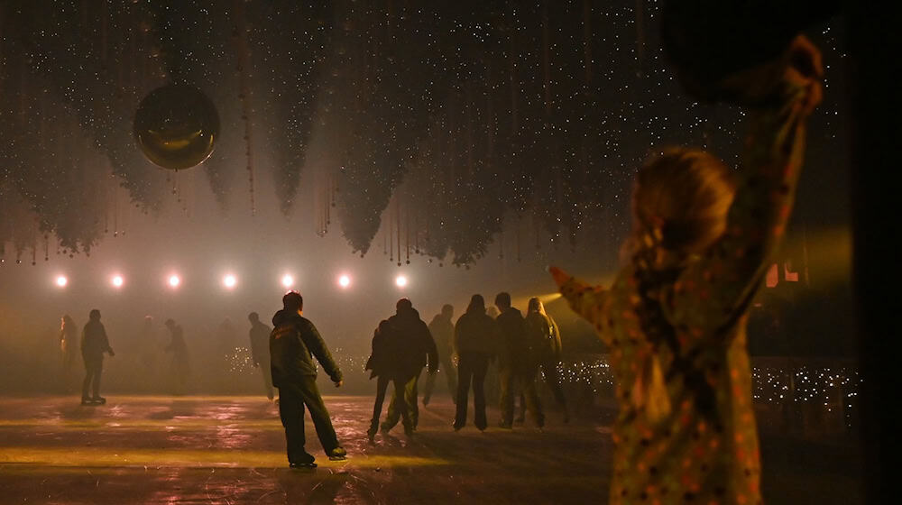 Besucher laufen auf der Eisfläche der Kunst-Lichtinstallation „Dark Matter: Forest Winterlights“.  / Foto: Elisa Schu/dpa