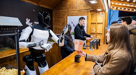 Der humanoide Roboter «Optimus» von Tesla verteilt bei seiner Vorstellung in der Mall of Berlin Popcorn an eine Besucherin. / Foto: Christoph Soeder/dpa